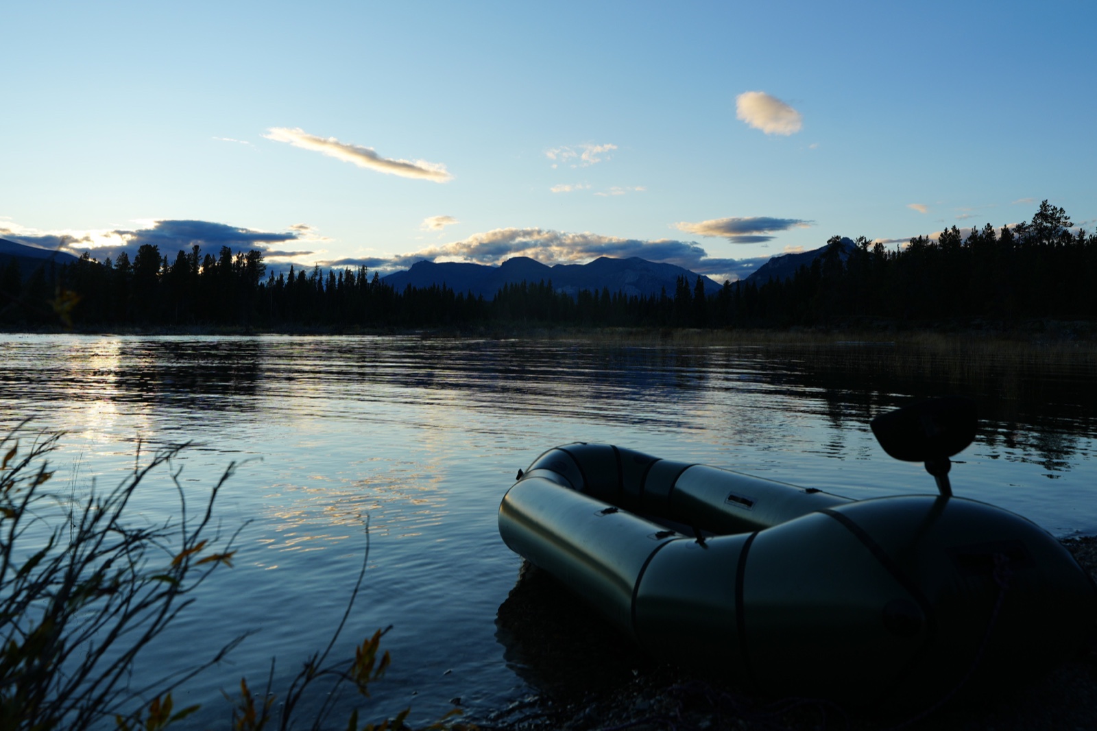 Packraft au bord d’une rivière face aux montagnes au coucher du soleil